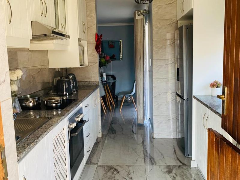 Modern galley-style kitchen featuring granite countertops, built-in oven, electric hob, extractor fan, and polished marble-look floor tiles.