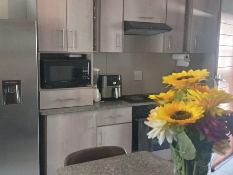 A functional kitchen featuring light-toned cabinetry, granite countertops, and integrated appliances, with direct access to an outdoor balcony area.