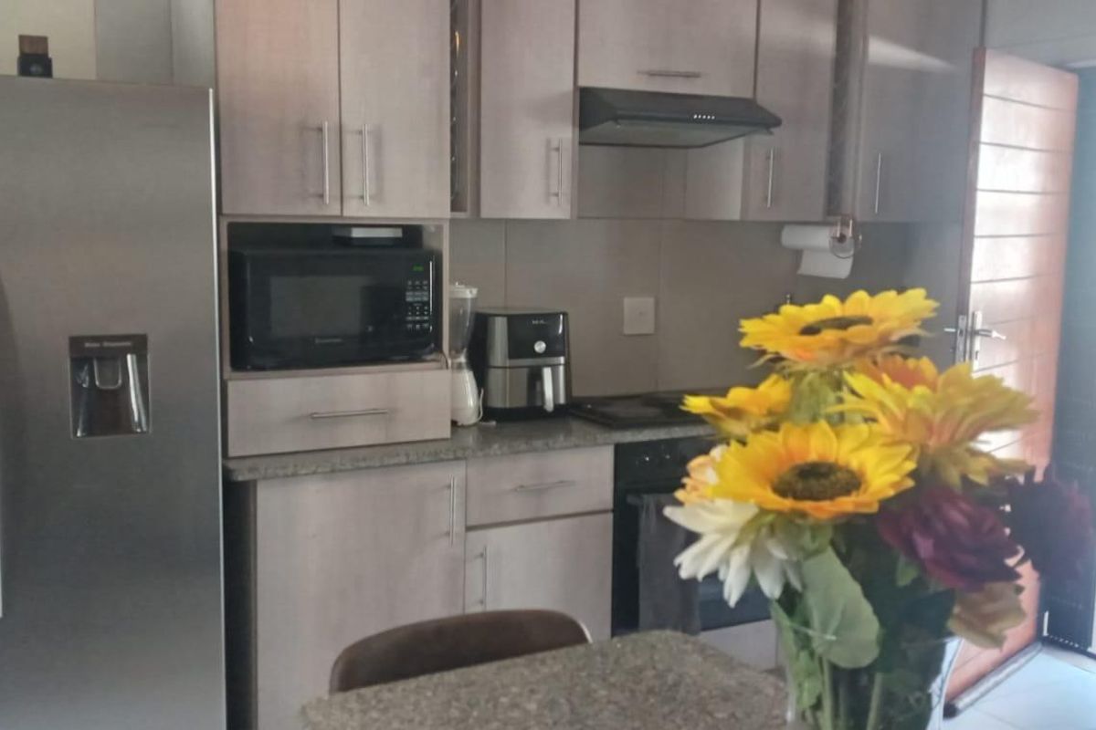 A functional kitchen featuring light-toned cabinetry, granite countertops, and integrated appliances, with direct access to an outdoor balcony area.