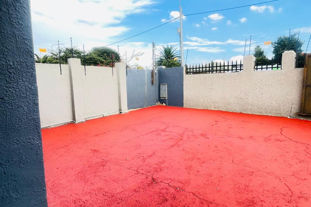 An outdoor paved area featuring a bright red surface finish, enclosed by perimeter boundary walls with integrated electric fencing.
