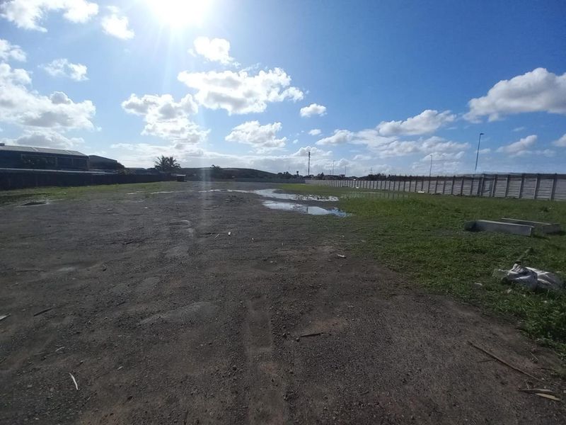 A large, undeveloped industrial plot featuring an unpaved surface and enclosed by a precast concrete boundary wall.