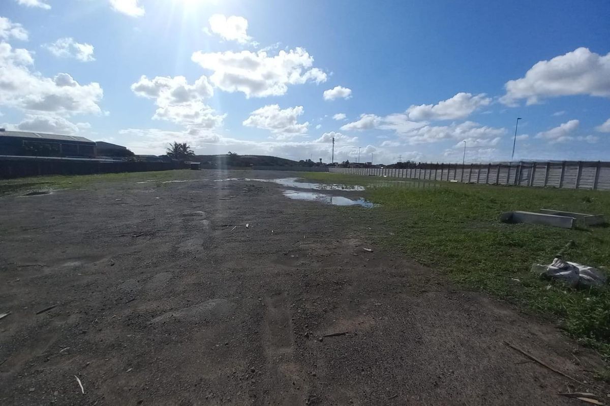 A large, undeveloped industrial plot featuring an unpaved surface and enclosed by a precast concrete boundary wall.