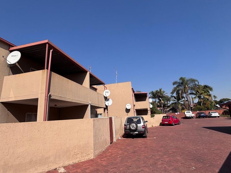 Exterior view of the apartment complex featuring paved driveway, covered parking areas, and private balconies with satellite dish installations.
