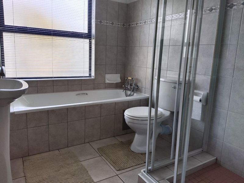 A functional bathroom featuring a pedestal basin, built-in bathtub, separate shower enclosure, and neutral ceramic tiling throughout.