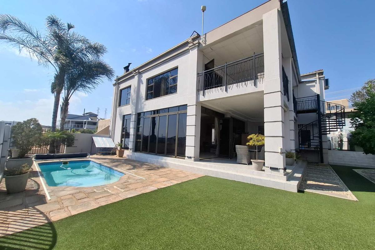 Rear view of a multi-story house featuring a swimming pool, covered patio, upper-level balcony, and a spiral staircase leading to the garden area.