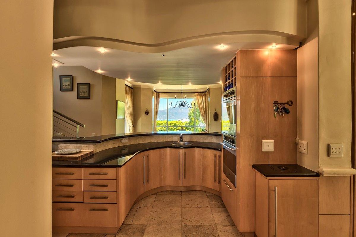 A well-appointed kitchen featuring curved wooden cabinetry, granite countertops, built-in oven, and stone flooring, with an open-plan layout overlooking a scenic view.