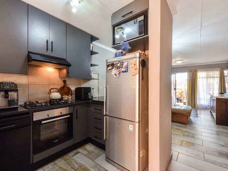 Modern open-plan kitchen featuring dark grey cabinetry, gas hob, built-in oven, and tiled flooring, seamlessly flowing into the adjacent living area.