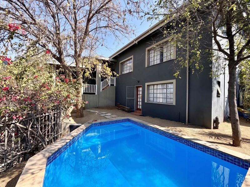 Rear exterior view featuring a swimming pool with tiled coping, adjacent to a two-story dwelling with dark painted facade and external staircase access.
