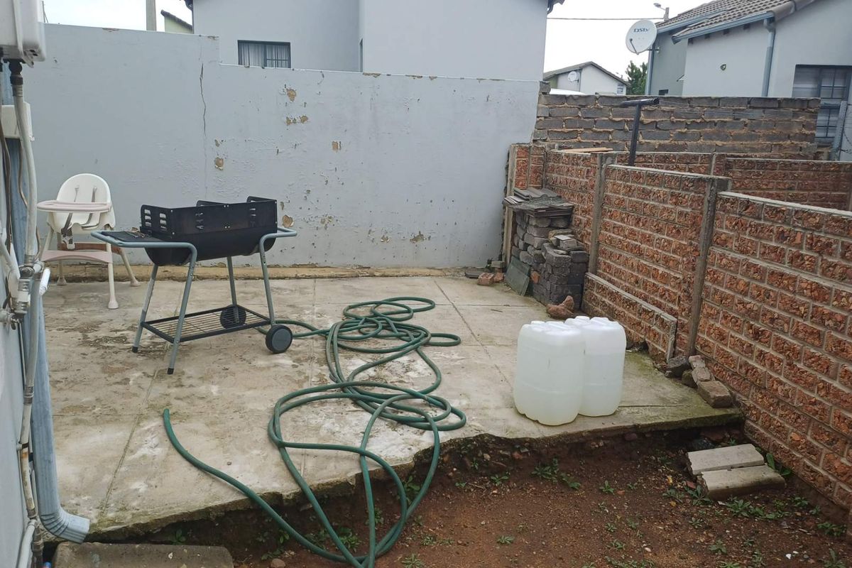 A small rear outdoor patio area featuring concrete paving, enclosed by brick and plastered boundary walls, requiring maintenance and landscaping.
