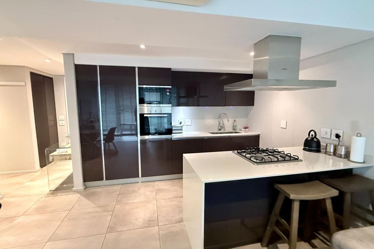 Modern kitchen featuring dark high-gloss cabinetry, stone countertops, a central island with a gas hob, and integrated stainless steel appliances.