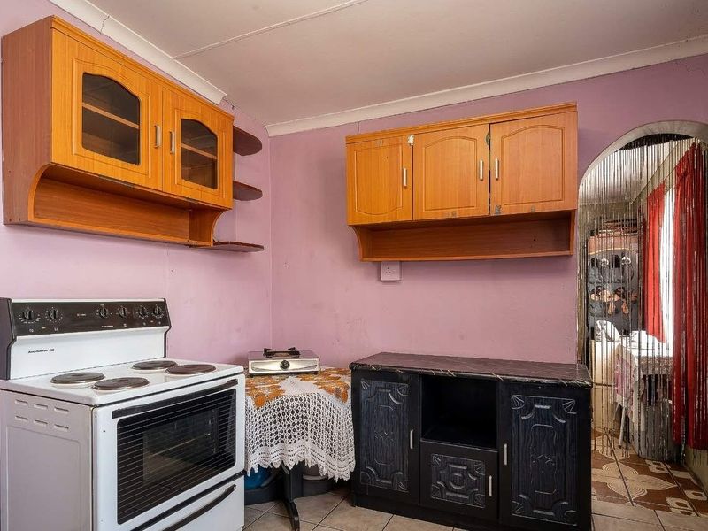 A compact kitchen featuring dated wooden cabinetry, a freestanding stove, and tiled flooring, offering potential for modernization and cosmetic updates.