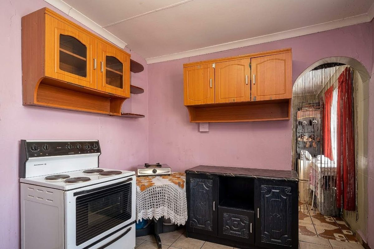 A compact kitchen featuring dated wooden cabinetry, a freestanding stove, and tiled flooring, offering potential for modernization and cosmetic updates.