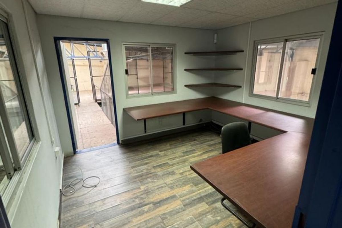 A functional office space featuring built-in corner desk, floating shelving, suspended ceiling with recessed lighting, and durable laminate flooring.