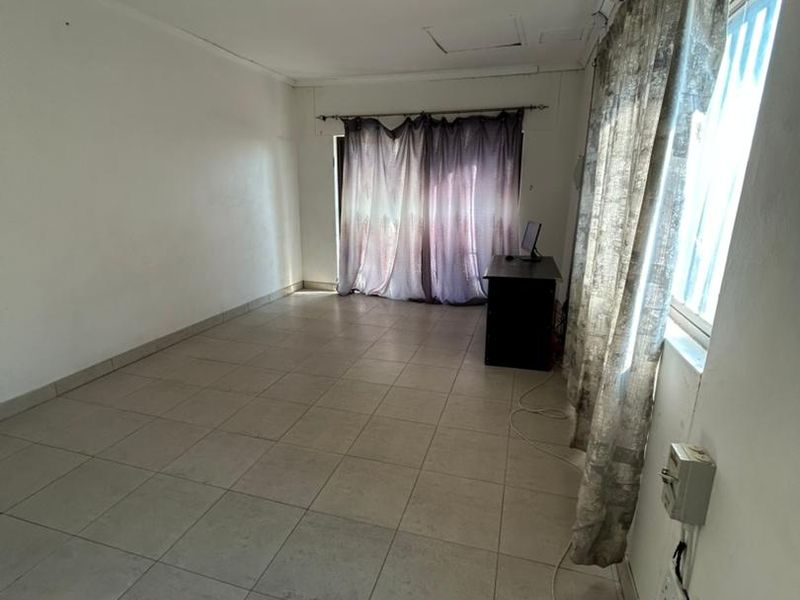 An empty living room featuring tiled flooring, a wall-mounted air conditioner, and basic lighting, ready for renovation or staging.