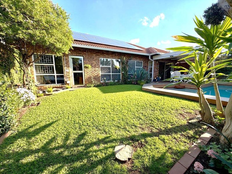 Rear view of the townhouse featuring a brick facade, solar panels, a well-maintained garden, and a swimming pool with a wooden deck.