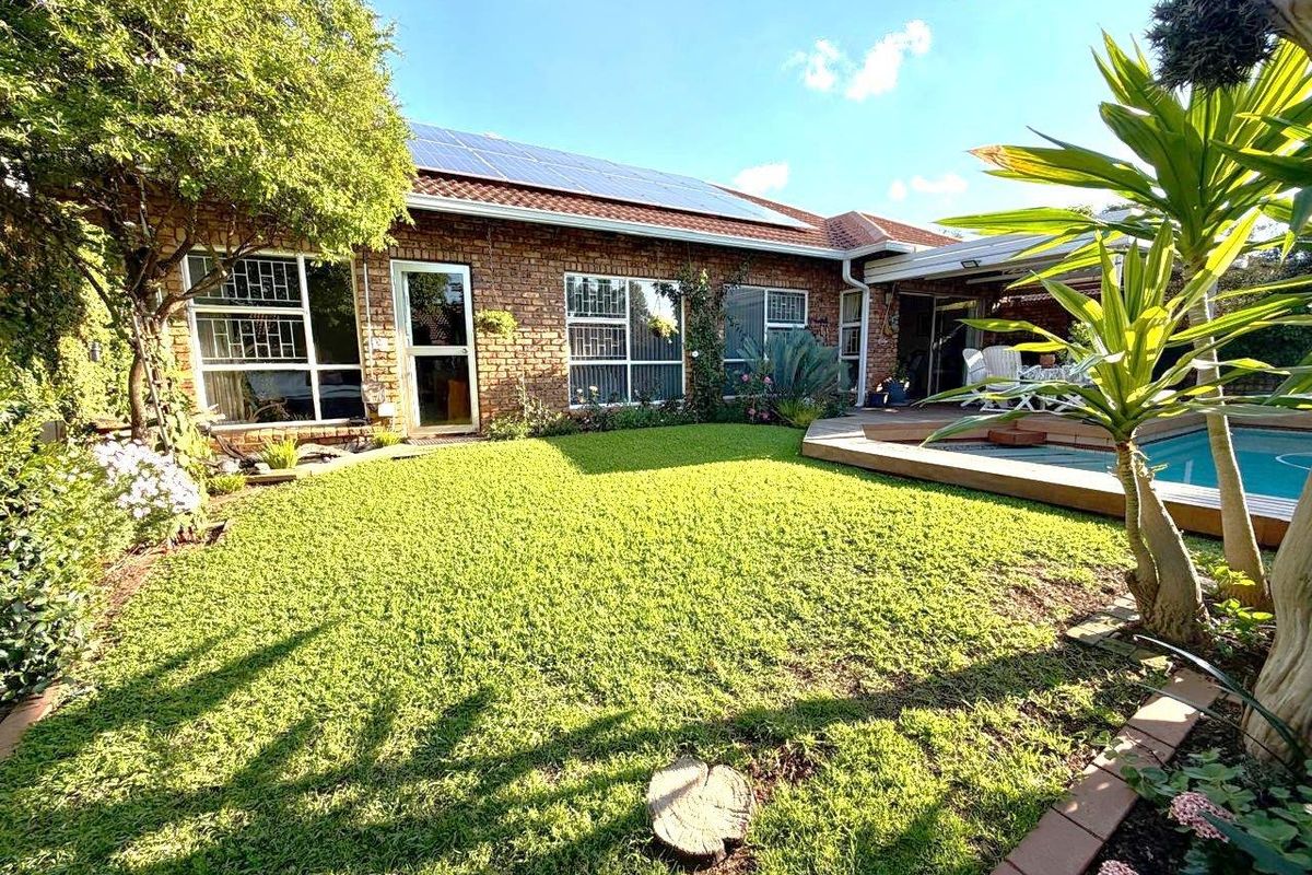 Rear view of the townhouse featuring a brick facade, solar panels, a well-maintained garden, and a swimming pool with a wooden deck.