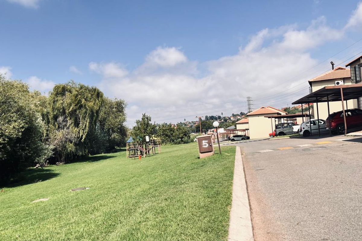 View of the apartment complex grounds featuring a communal lawn area, paved driveway, and covered parking structures.