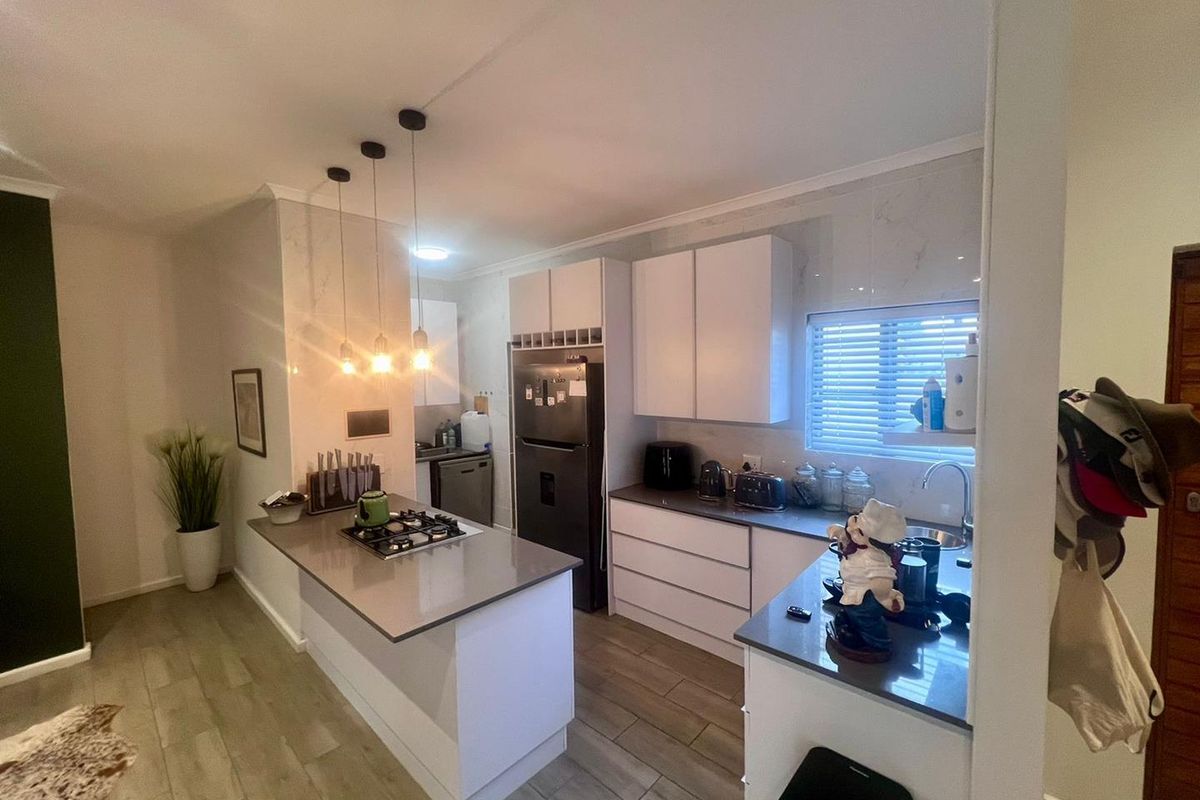 Modern kitchen featuring stone countertops, a gas hob, sleek white cabinetry, and contemporary pendant lighting, creating a functional and stylish cooking space.