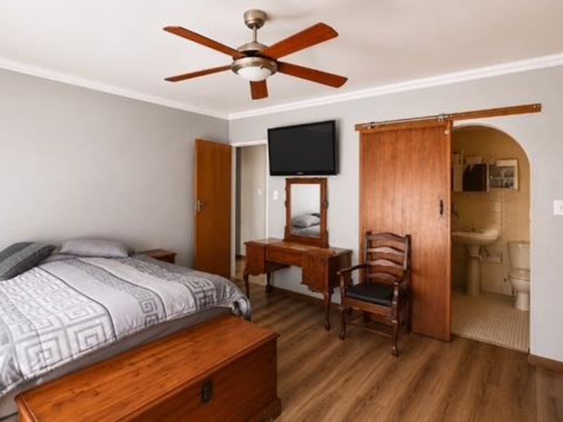 Spacious bedroom featuring laminate flooring, a ceiling fan, built-in cupboards, and a sliding barn door leading to an en-suite bathroom.