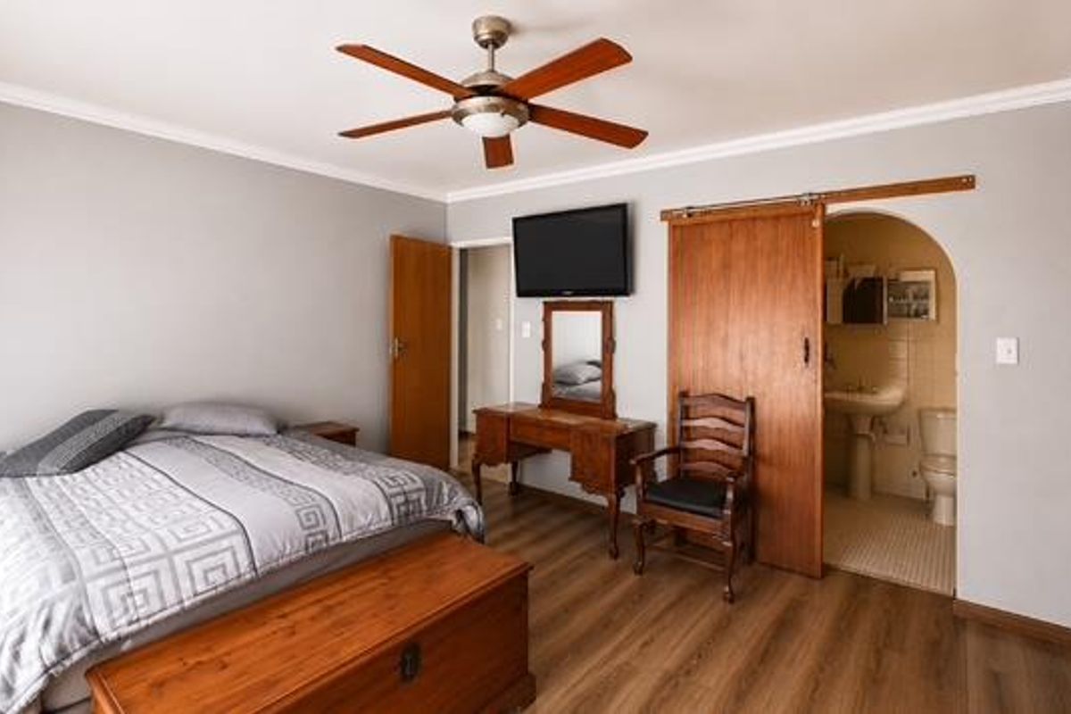Spacious bedroom featuring laminate flooring, a ceiling fan, built-in cupboards, and a sliding barn door leading to an en-suite bathroom.