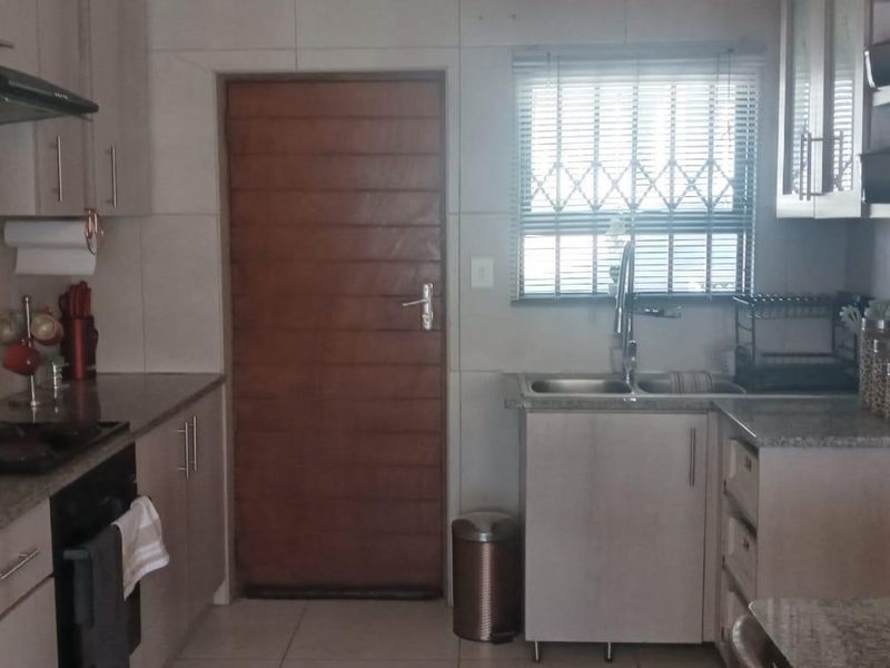 A functional kitchen featuring light-toned cabinetry, granite countertops, a double sink, and integrated appliances, with tiled flooring and a secure window.