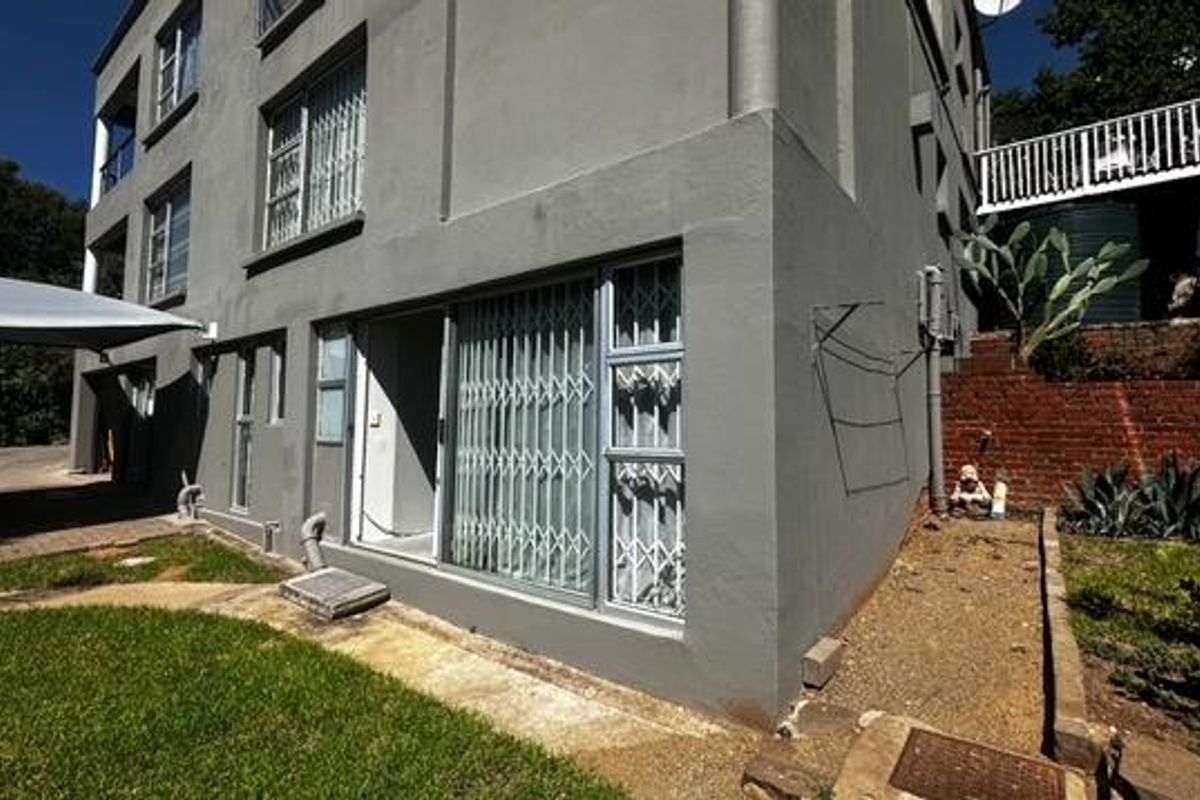 Exterior view of the multi-story residential building featuring sliding glass doors with security gates, a paved walkway, and a brick retaining wall.