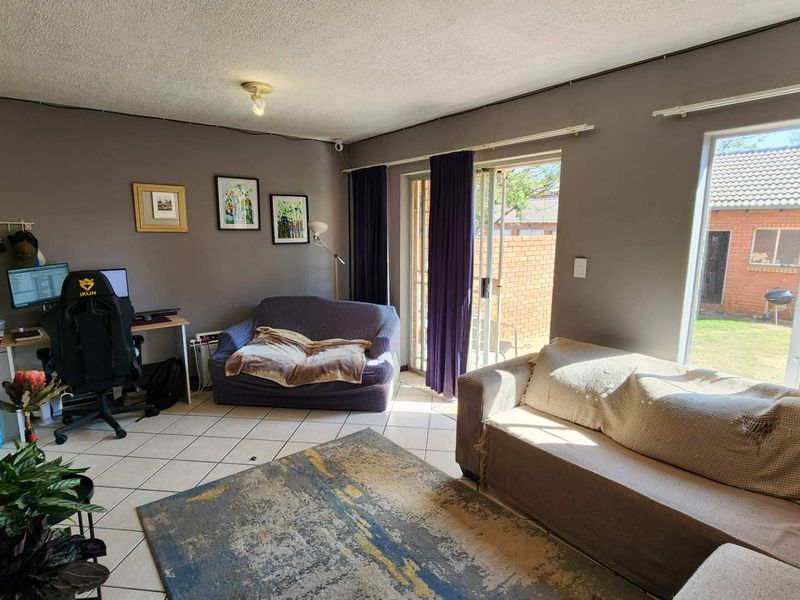 A living room featuring tiled flooring, large windows, and a sliding glass door providing access to the rear garden area.