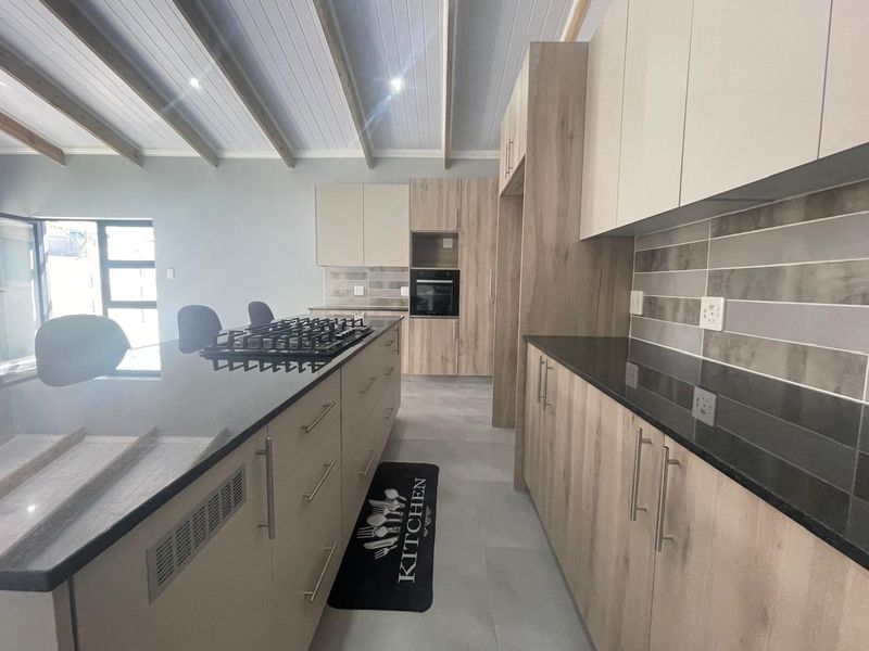 Modern kitchen featuring light wood cabinetry, dark stone countertops, a central island with a gas hob, and an exposed beam ceiling.