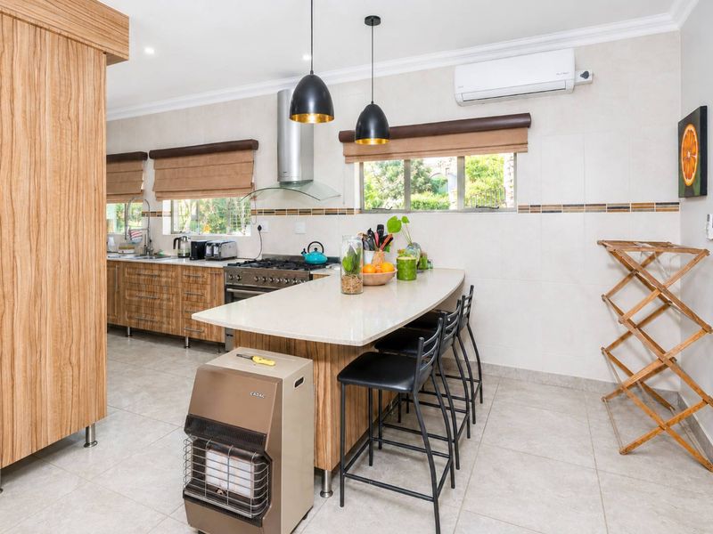 Modern kitchen featuring a central island with stone countertops, gas stove, extractor fan, and ample built-in cabinetry, complemented by tiled flooring and air conditioning.