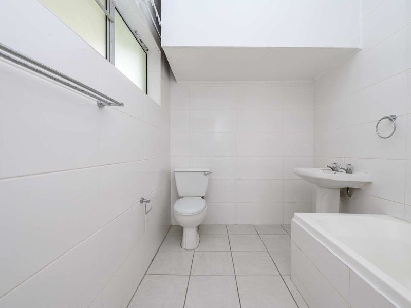 A clean, functional bathroom featuring a pedestal basin, toilet, and bathtub with white wall and floor tiling throughout.