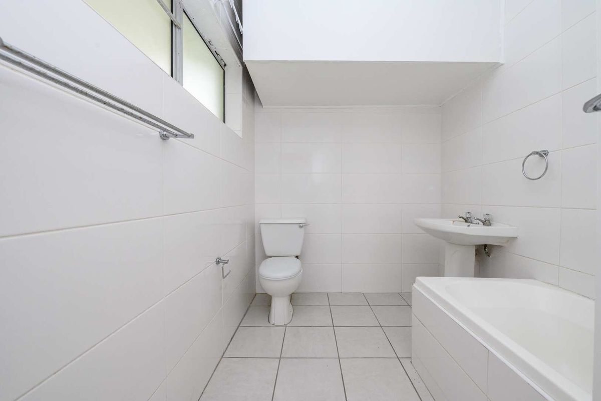 A clean, functional bathroom featuring a pedestal basin, toilet, and bathtub with white wall and floor tiling throughout.