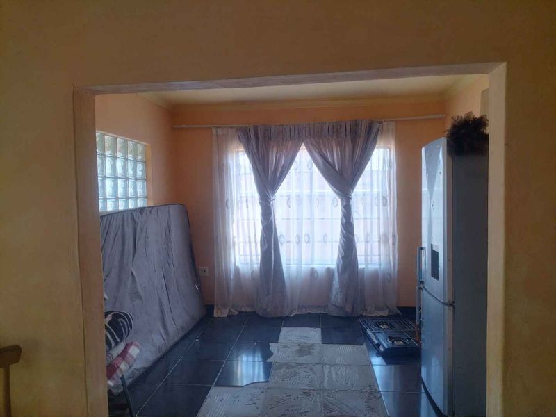 A living area featuring tiled flooring, a glass block window, and natural light, currently requiring cosmetic updates and floor finishing.