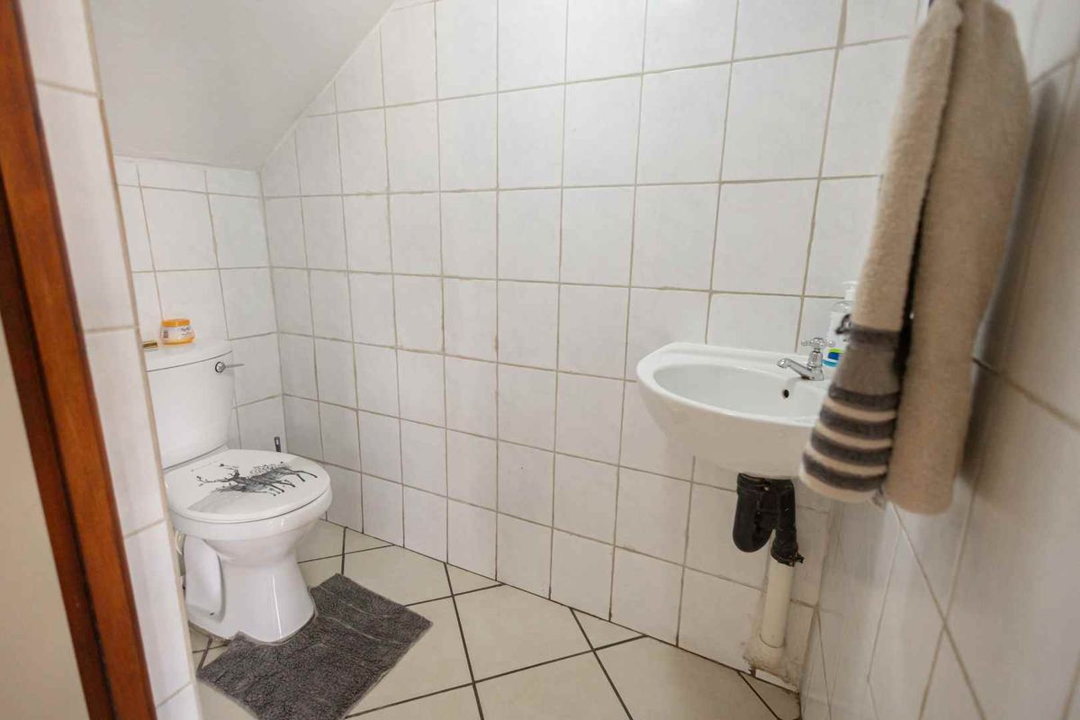 A compact guest bathroom featuring white wall tiles, a pedestal basin, and a standard toilet, situated under a sloped ceiling.