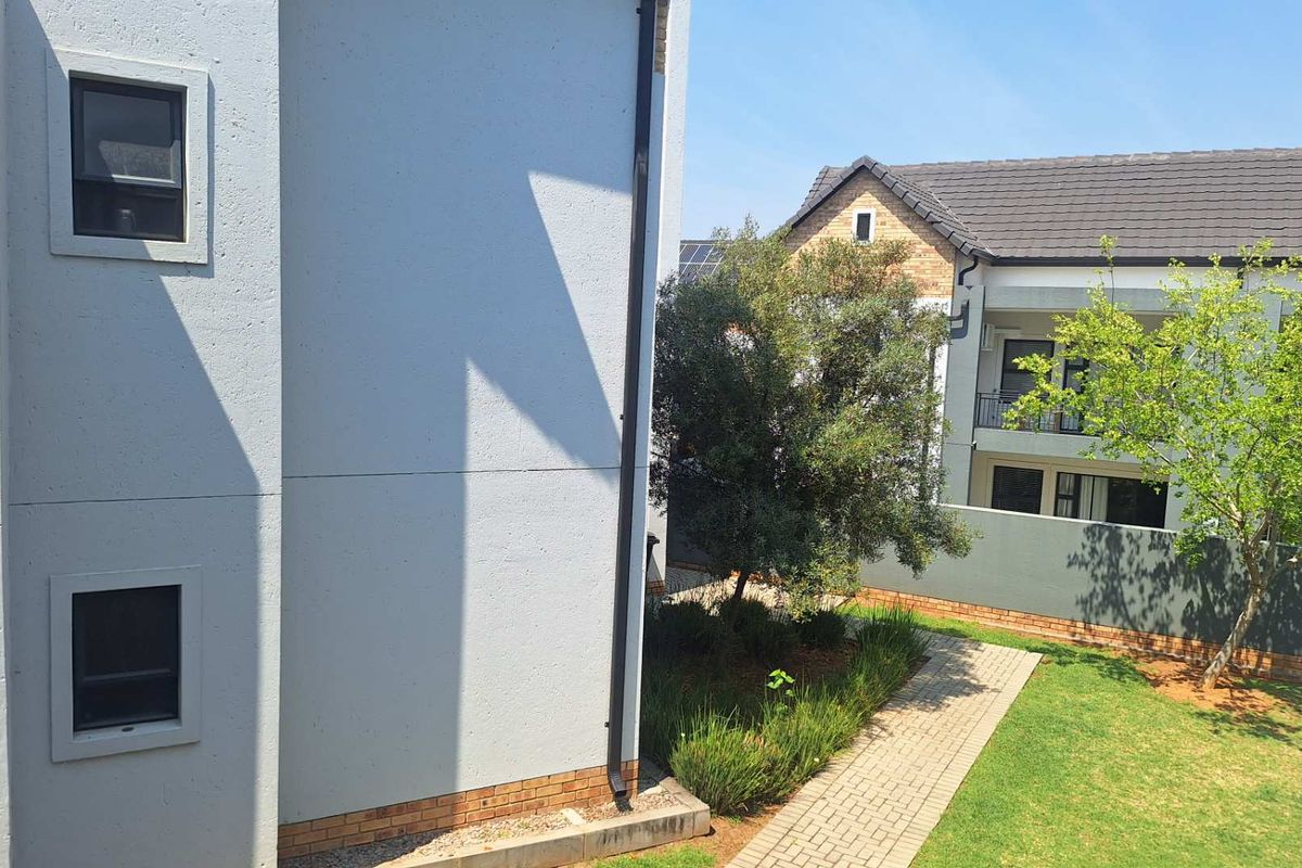 A view of the rear exterior area featuring a paved walkway, landscaped garden, and modern apartment building architecture with a tiled roof.