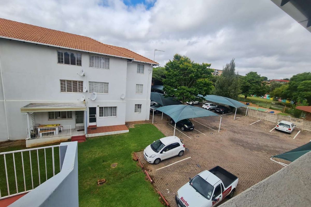Elevated view of the apartment complex rear exterior, featuring a paved parking area with shade cloth carports and a communal lawn.
