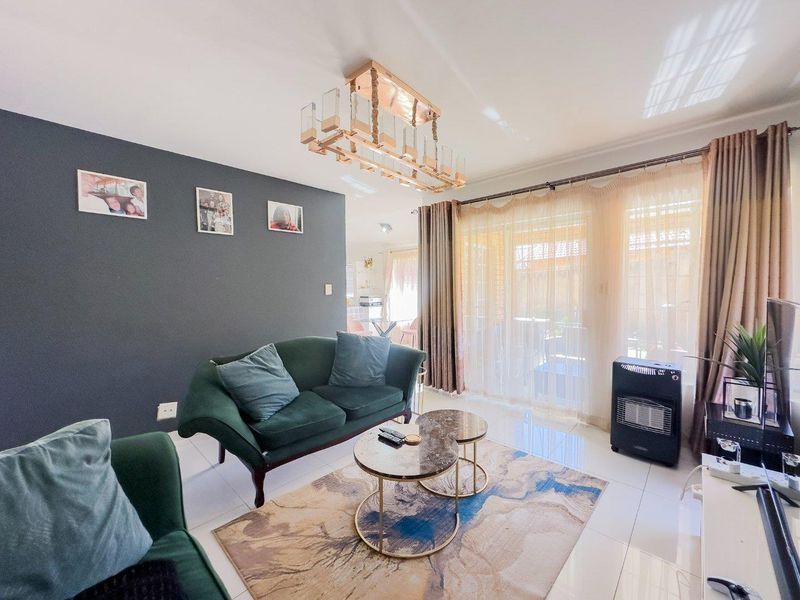 A bright living room featuring tiled flooring, a modern feature light fixture, and large sliding glass doors providing access to the outdoor area.