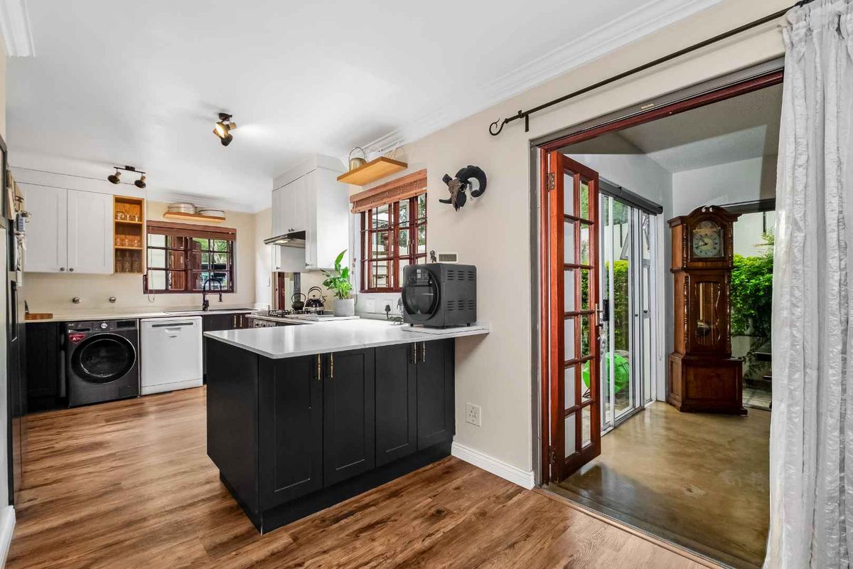 Modernized kitchen featuring dark cabinetry, stone countertops, integrated appliances, and direct access to an outdoor patio area through timber-framed glass doors.
