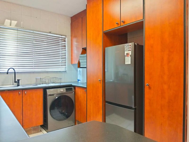 A functional kitchen featuring wood-look laminate cabinetry, dark countertops, a tiled backsplash, and dedicated space for laundry and refrigeration appliances.