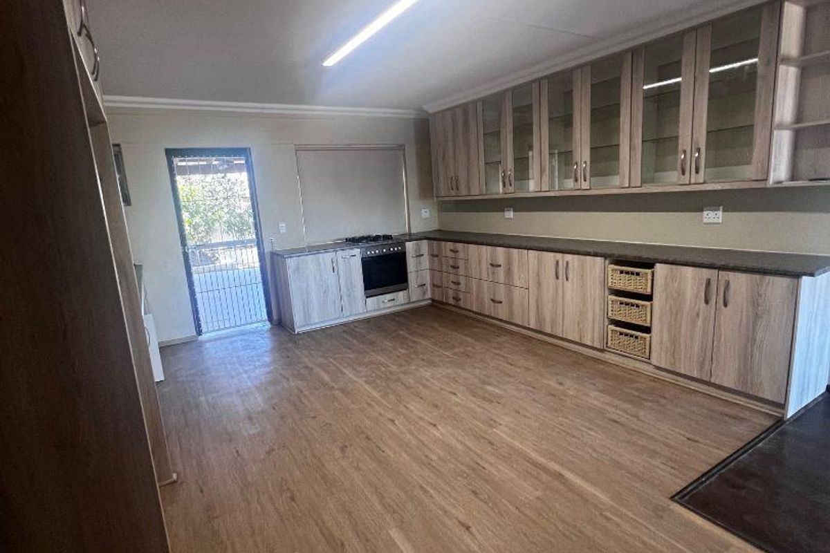 Spacious kitchen featuring extensive light wood cabinetry, dark countertops, integrated oven and hob, and durable wood-look flooring with direct exterior access.