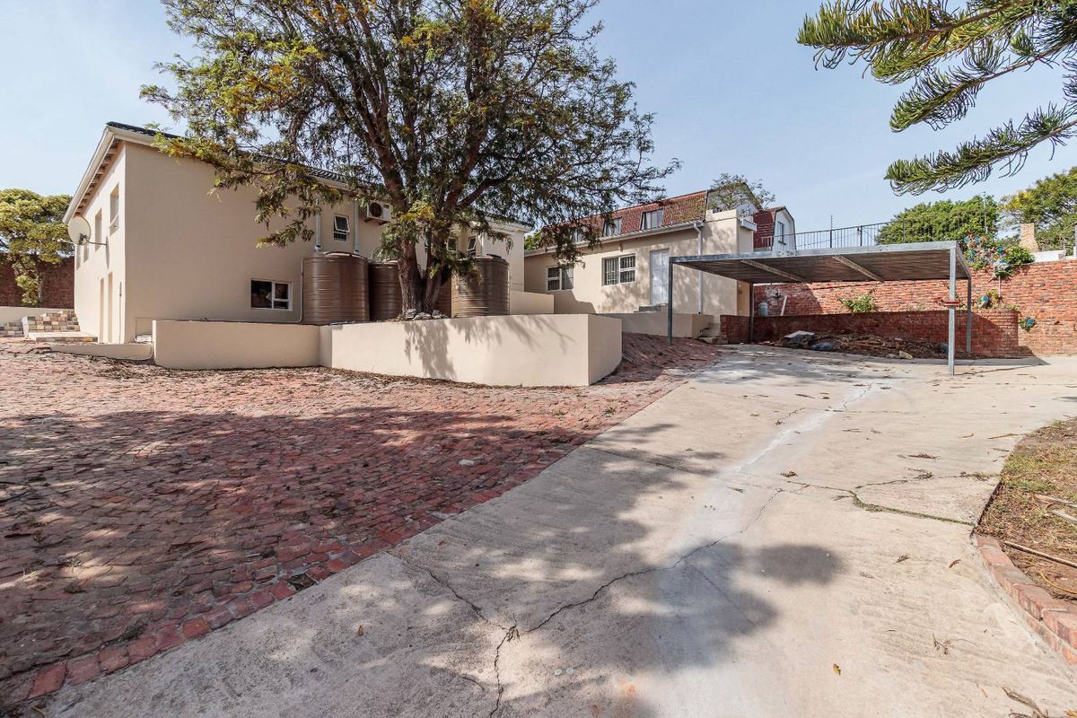 Rear exterior view featuring a large tree, water storage tanks, a carport, and a combination of brick and concrete driveway surfaces.