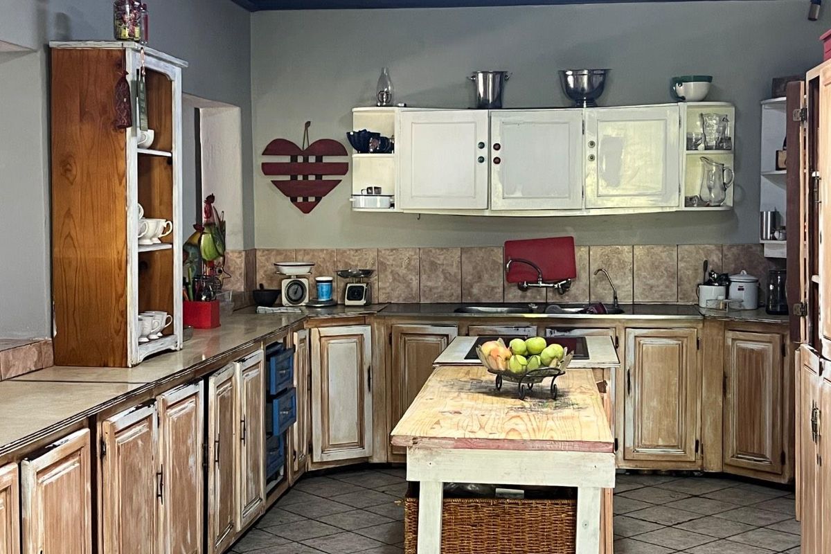 A rustic-style kitchen featuring wooden cabinetry, a central island, tiled backsplash, and integrated sink fixtures.