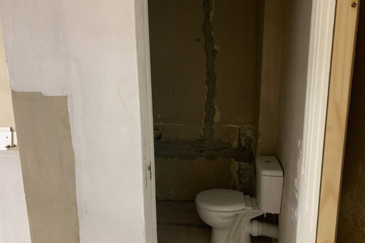 A small bathroom in need of renovation, featuring a standard toilet and unfinished wall surfaces requiring plastering and painting.