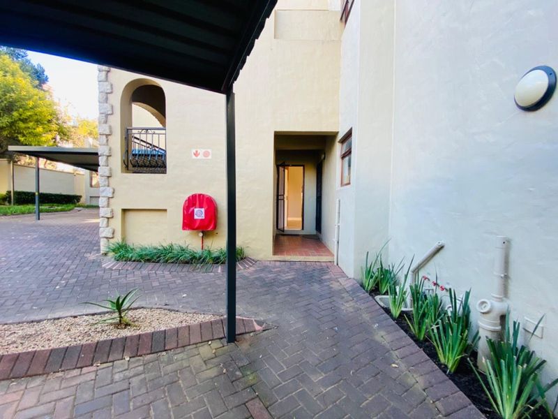Exterior view of the apartment entrance featuring a paved walkway, covered access, and building facade with stone detailing and fire safety equipment.