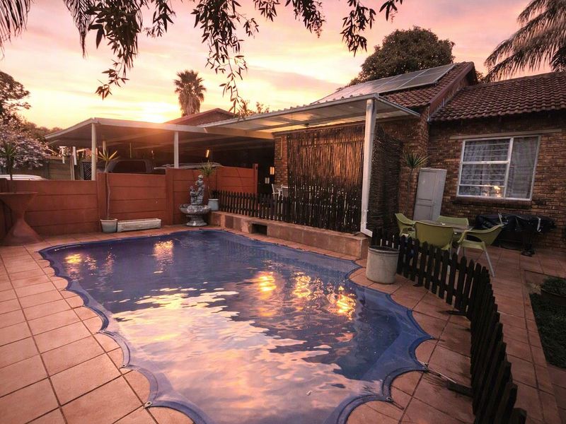 Outdoor pool area featuring a tiled patio, brick townhouse exterior, and solar panels, set against a sunset backdrop.