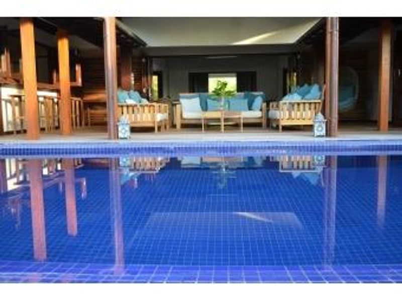 A view of a swimming pool with a covered patio area featuring timber structural columns and open-plan outdoor living space.