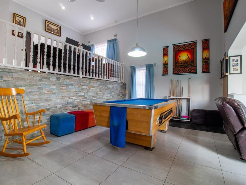 Spacious living area featuring a stone-clad feature wall, white timber balustrade, tiled flooring, and recessed downlighting, creating a versatile entertainment space.