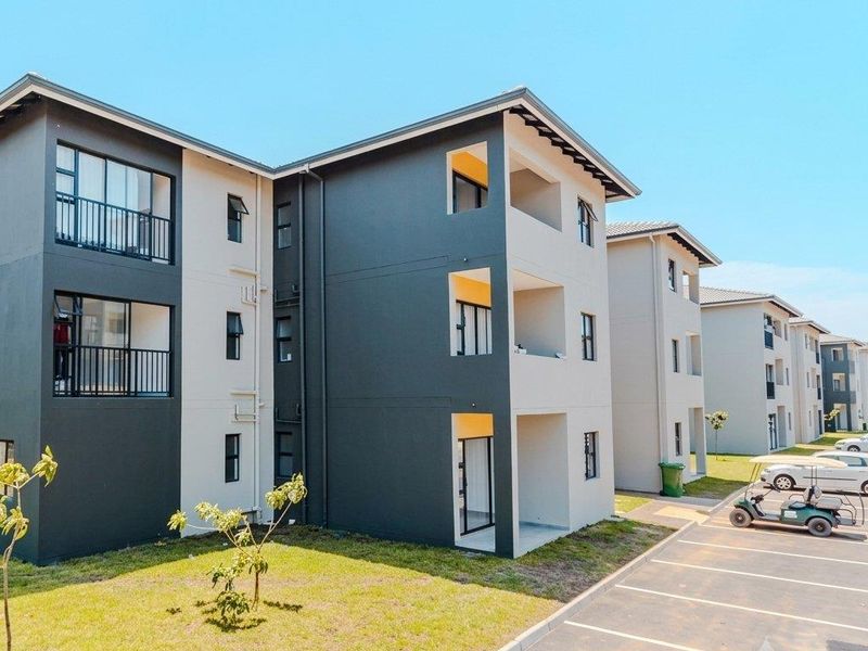 Modern apartment complex exterior featuring contemporary grey and white facade, private balconies, and dedicated paved parking spaces within a well-maintained residential estate.