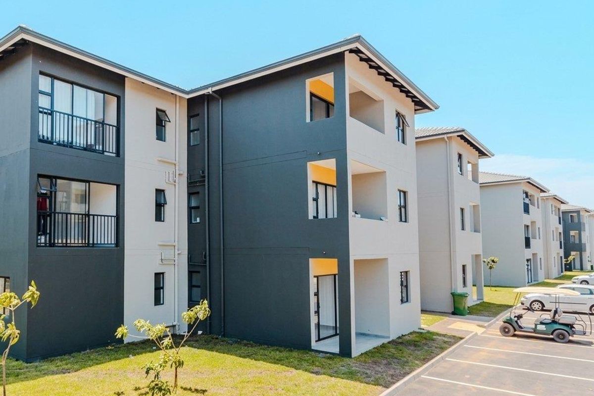 Modern apartment complex exterior featuring contemporary grey and white facade, private balconies, and dedicated paved parking spaces within a well-maintained residential estate.