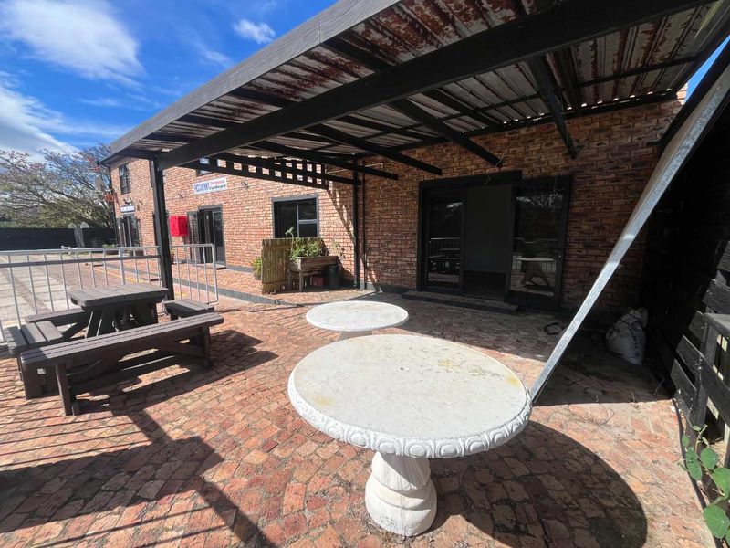 Outdoor patio area featuring brick paving, exposed brick walls, and a covered roof structure with steel supports, providing a functional exterior space.