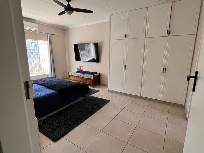 Spacious bedroom featuring neutral tiled flooring, extensive built-in cabinetry, a ceiling fan, and a wall-mounted air conditioning unit.